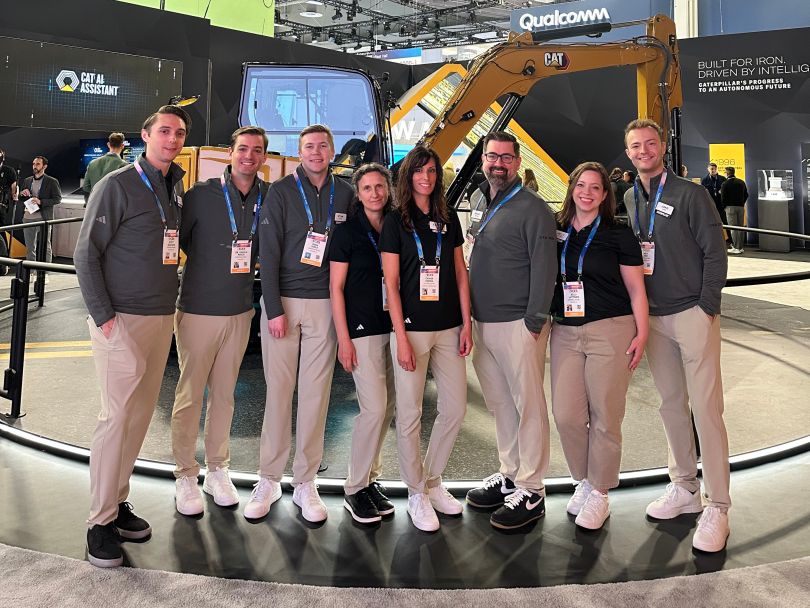 Director of Analytics Charlie Wood poses with several colleagues for a group photo in front of Caterpillar equipment during an industry convention